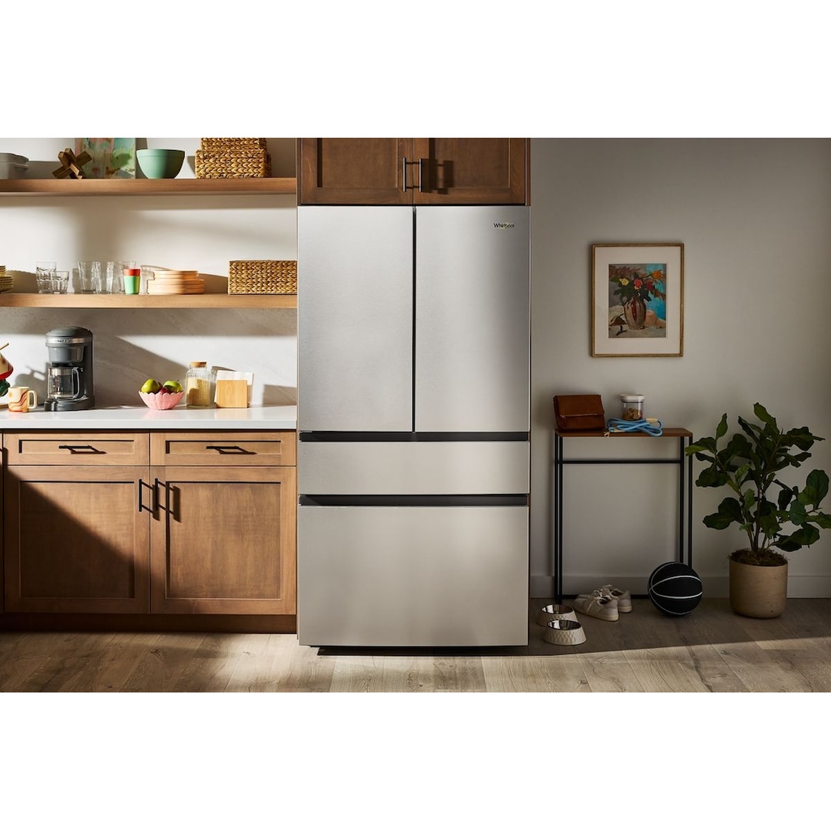 Whirlpool stainless steel French door refrigerator installed in a warm-toned family kitchen with wood cabinetry, open shelving, and natural light