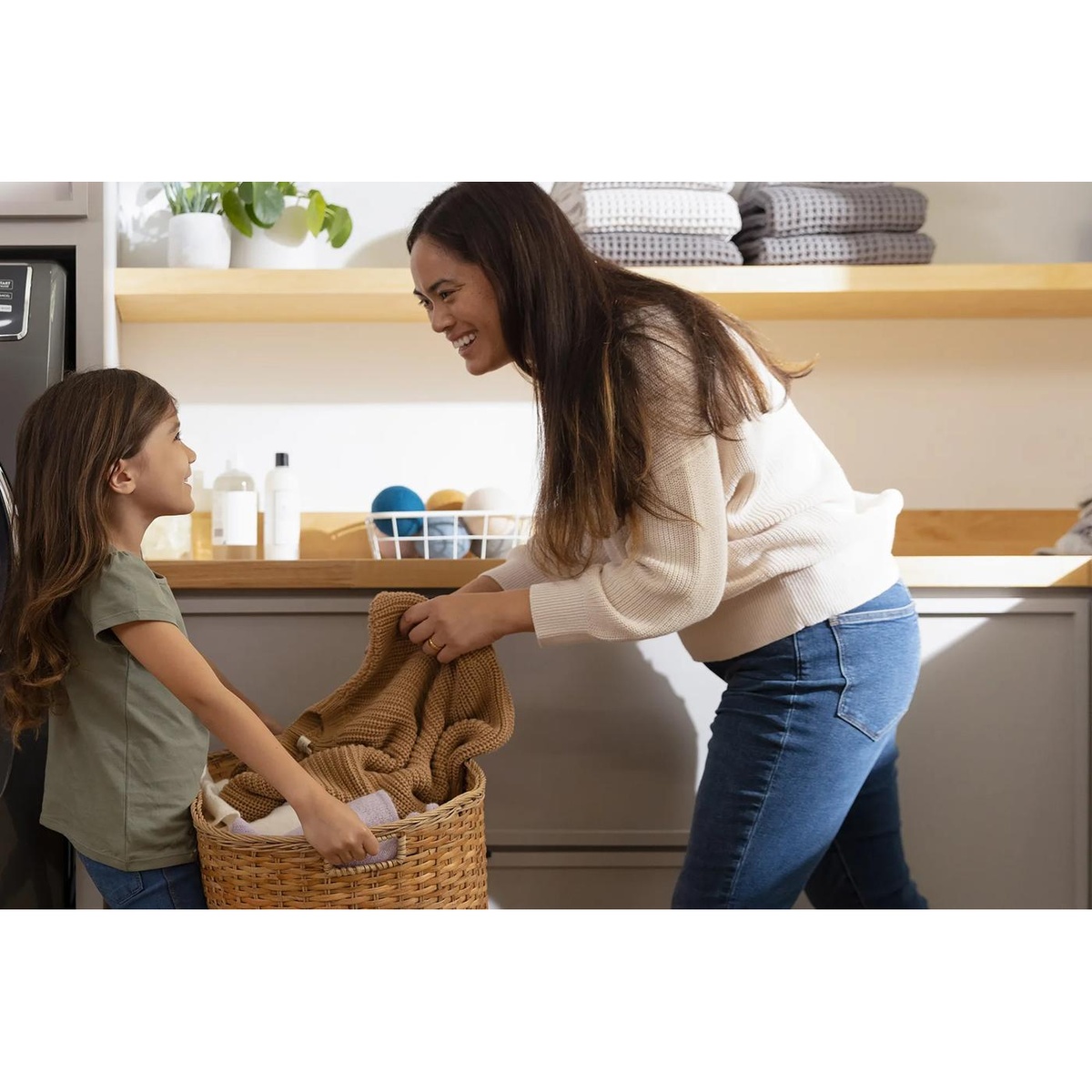 Parent and child carrying a laundry basket in a bright laundry room with an Electrolux laundry appliance nearby
