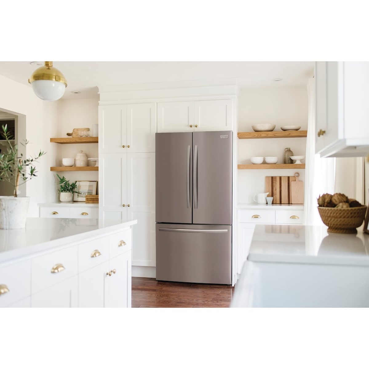 Stainless steel French door refrigerator installed in a bright white kitchen with open wood shelves