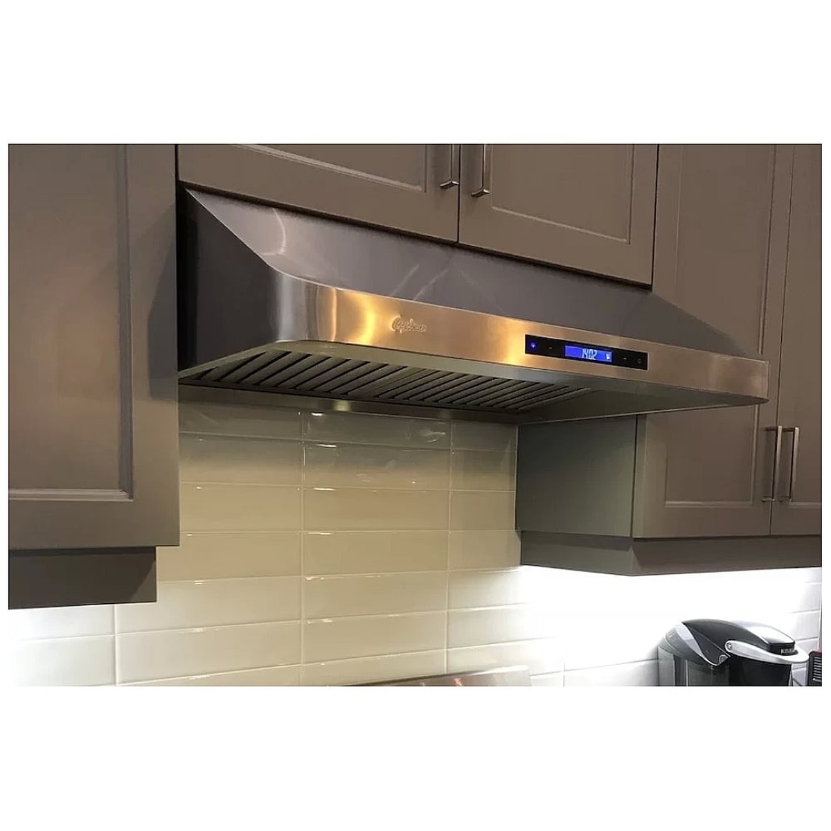 Stainless under-cabinet range hood installed between kitchen cabinets with lights on and a digital display