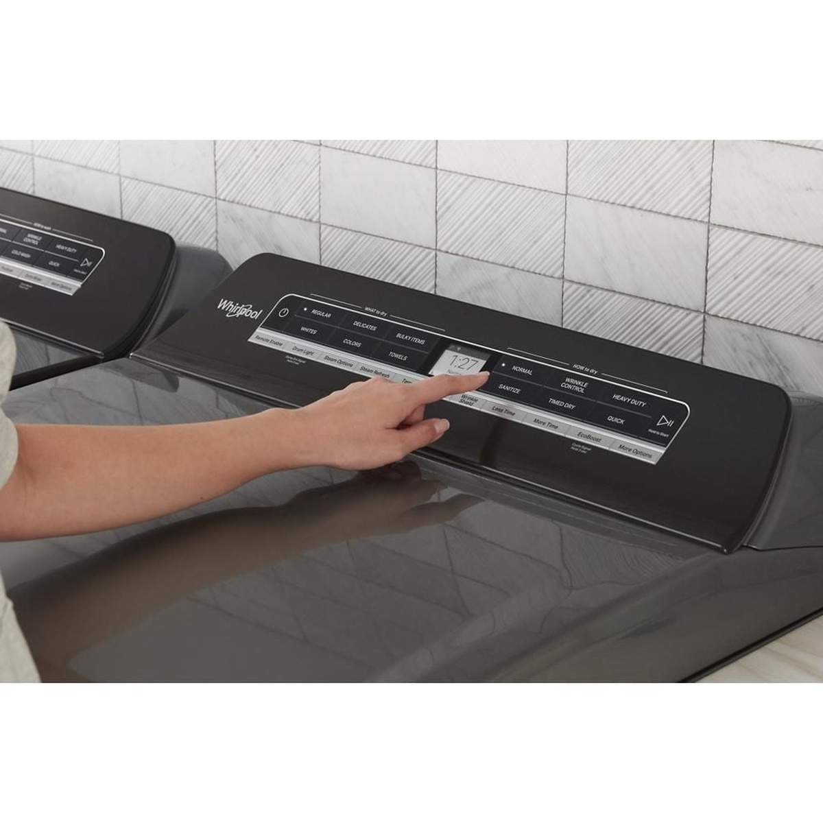 Hand using the Whirlpool dryer top touch control panel with cycle labels and a digital time display