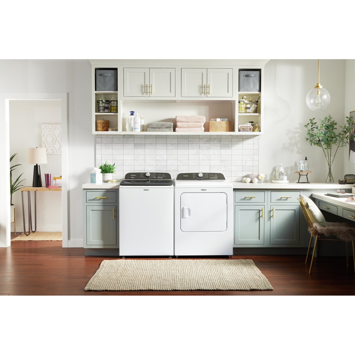 Whirlpool washer and dryer installed side by side in a bright laundry room with cabinets, countertop, and decor.