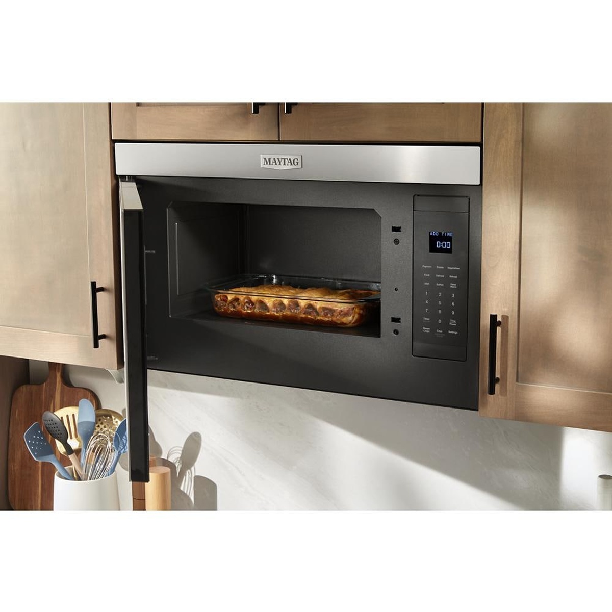 Maytag over-the-range microwave installed in cabinetry with the door open, showing the interior cavity, a large baking dish, and the right-side control panel